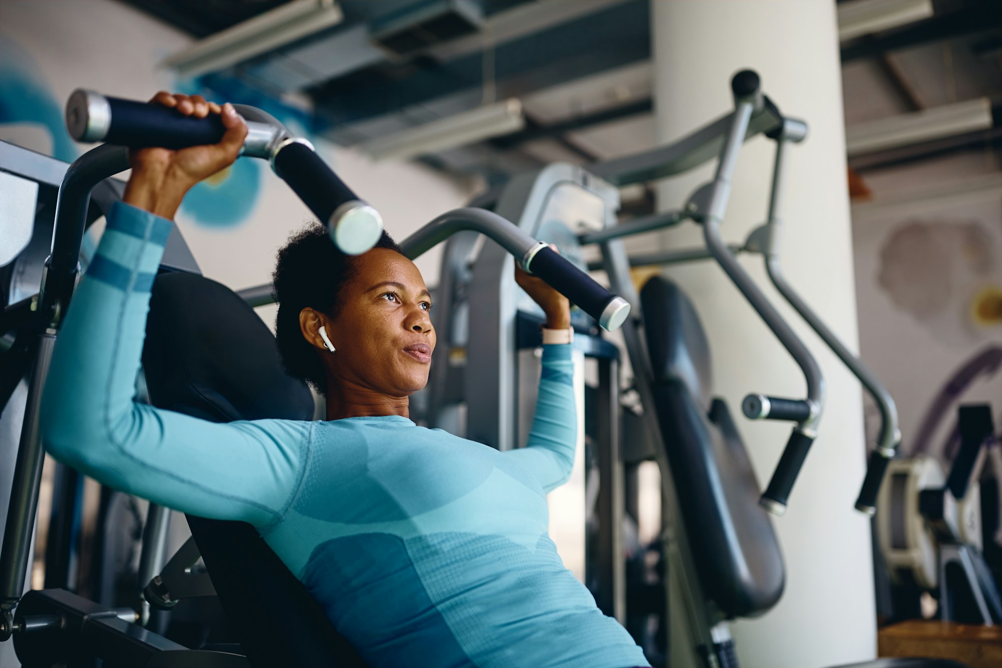 African American athletic woman using exercise machine during sports training in health club.